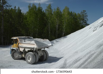 Heavy Mining Truck Loaded With Crushed Stone Stands Against A Hill Of Crushed Stone And A Green Forest In Sunny Weather. Mining Industry.