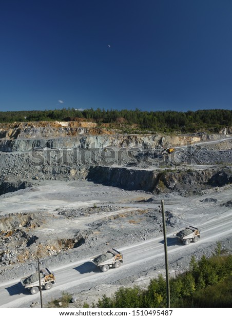 Heavy mining trucks transport ore in a stone\
quarry, top view, vertical\
panorama.