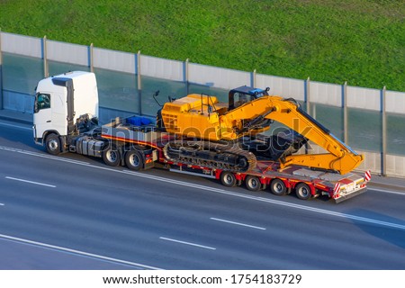 Heavy new yellow excavator on transportation truck with long trailer platform on the highway in the city