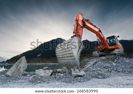 heavy organge excavator with shovel standing on hill with rocks