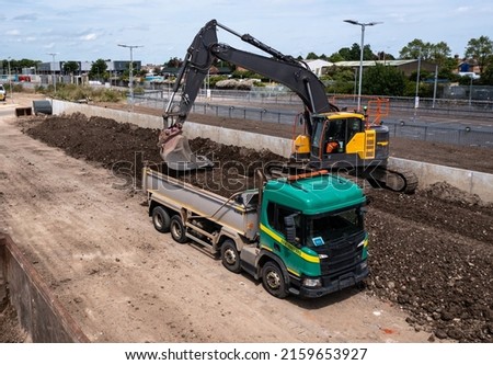 A heavy plant digger machine loading a tipper lorry with spoil from a railway engineering sidings