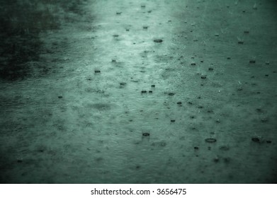 Heavy rain, droplets splashing on pavement. Green tint