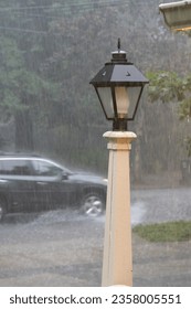 Heavy rain falling, bouncing off pavement, car splashing, lamppost in foreground