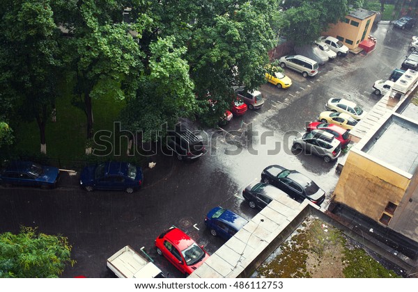 Heavy rain falling in city in a summer day, wet street\
and parked cars 