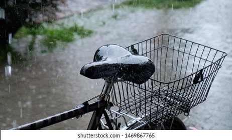 Heavy rain falling on a bicycle seat parked on sidewalk.  Focus on the seat, with rest heavily defocussed