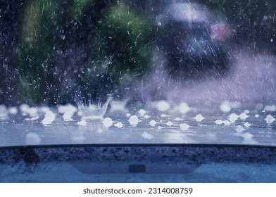 Heavy rain with hail hits the roof of the car. Splashes and fragments of ice are blurred in motion. The concept of auto insurance and natural disasters. Driving on rainy days. Selective focus. - Shutterstock ID 2314008759