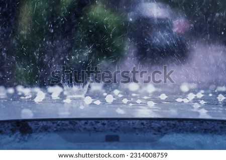 Heavy rain with hail hits the roof of the car. Splashes and fragments of ice are blurred in motion. The concept of auto insurance and natural disasters. Driving on rainy days. Selective focus.