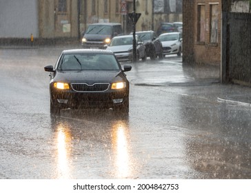 Heavy rain storm and flooded roads cars driving in downpour lights on reflecting in water of city streets. Flooding and risk of aquaplaning standing water on tarmac. Dark and moody torrential weather