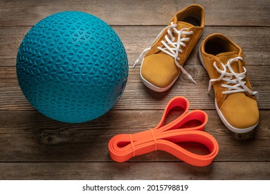 Heavy Rubber Slam Ball Filled With Sand, Resistance Band And Minimalist Barefoot Sneakers On A Rustic Wooden Deck, Exercise And Fitness Concept