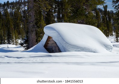 Heavy snowfall covering the whole hut. Fabulous winter house covered with snow up to the roof in the mountains. Untouched deep white pure snowdrifts in winter forest.