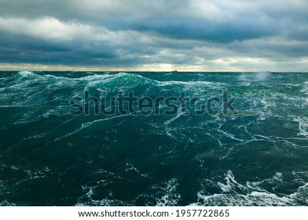 Heavy storm in the ocean. Big waves in the open sea, cloudy sky during a storm and a cargo ship on the horizon.
