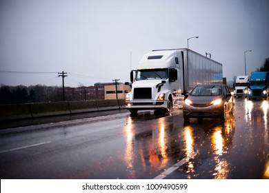 Heavy traffic with big rig semi trucks convoy with semi trailers transporting commercial cargo and another cars on highway in rain evening with headlight reflection on wet surface