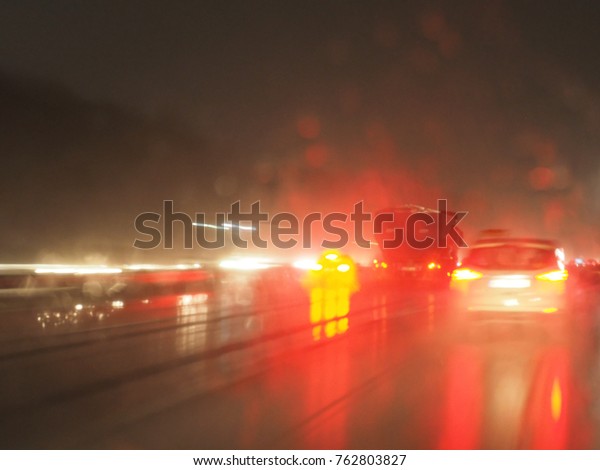 Heavy traffic on the\
highway at night and in rain: wet front window, red taillights,\
light reflections