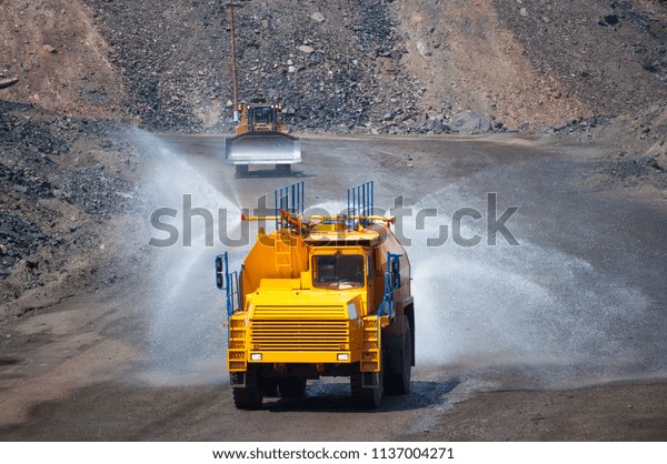 Heavy truck pours the road with water in the iron\
ore quarry. Dust removal, protection of the environment. Irrigation\
of the road from dust