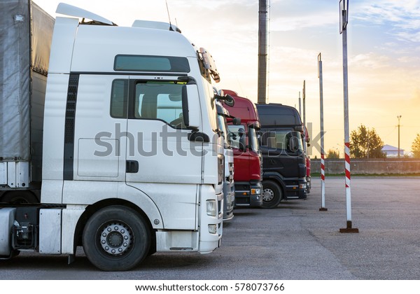 Heavy\
trucks loaded with goods trailers, parked in waiting area on state\
border crossing. International hard transportation and logistics.\
Transport infrastructure in evening at\
sunset