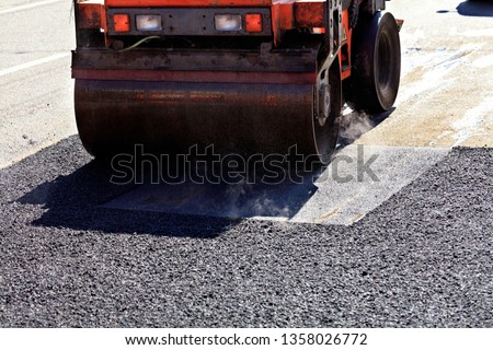 A heavy vibratory road roller compacts asphalt on the repaired stretch of road.