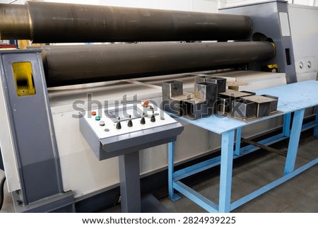 Heavy-duty four-roll bending machine forms metal plates; industrial control panel enables precise operation. Steel profile samples on blue workbench highlight fabrication workflow in a production sett