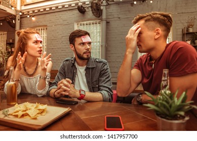 A hedbanz game. Beaming active joyful nice-appealing attractive radiant glowing adult friends enjoying playing a hedbanz game at the bar