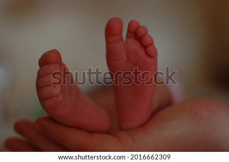 The heels of a baby in the hand of an adult. Dark, subdued light. blurred background