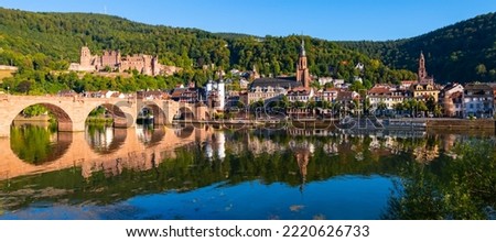 Heidelberg wide angle old town panorama with castle, “Karl Theodor Bridge“ and its twin tower gate, Church of the Holy Spirit. Reflection in the water of River Neckar on a sunny summer day in Germany.