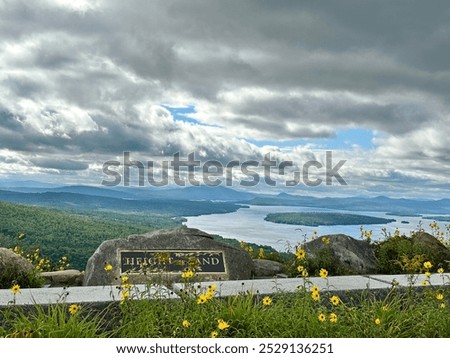 Height of the Land plaque and viewpoint in Rangeley, Maine. Overlook of Rangeley lake. Cloudy blue sky and yellow wildflowers. 