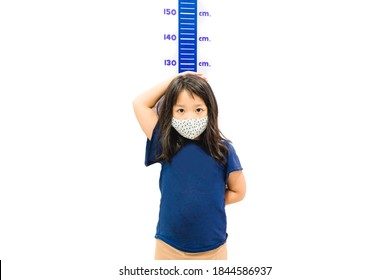 Height Measure Kid Girl Wearing Mask.Kid Measures The Growth Isolated White Wall.6 Years Old Girl Kid Standing Using Hand Measuring Her Height.Growth Hormones, Child Development, Calcium Supplements.