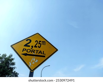 Height Restriction Traffic Sign with Clear Blue Sky. A bright yellow traffic sign indicating a height restriction of 2.25 meters (2,25m) with an arrow pointing to the left - Powered by Shutterstock