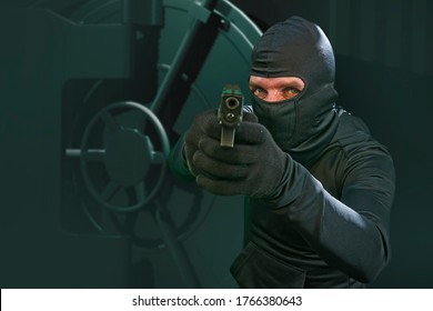 Heist And Robbery - Hollywood Style Portrait Of Man In Balaclava Mask Holding Gun In Front Of Security Metal Vault Door In Bank Or Casino Heist Concept Stealing Money Unlocking Safe