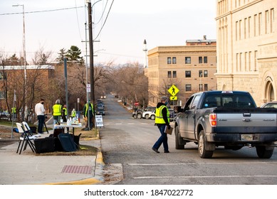 Helena, Montana / November 3, 2020: Election Day Voting At Polling Station Outside, Woman Poll Worker In Yellow Vest Wearing A Mask For Safety During Coronavirus Pandemic Speaking With Voter In Truck