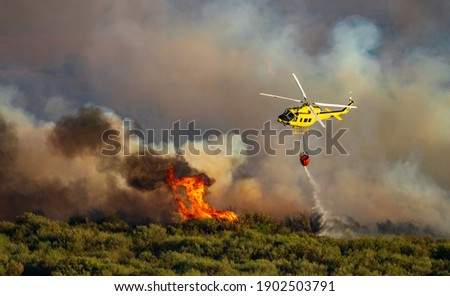 Helicopter with bambi bucket dumping water over the flames