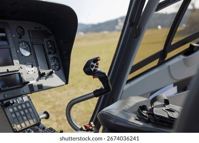 Helicopter cockpit features controls and instruments against a backdrop of an open grassy area and distant hills.
