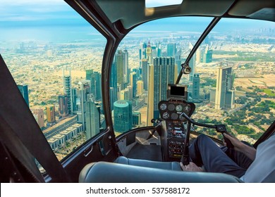 Helicopter cockpit flies in skyscrapers of Dubai downtown skyline on Sheikh Zayed Road, United Arab Emirates, with pilot arm and control board inside the cabin.