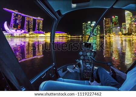 Helicopter cockpit interior flying on Panorama of Singapore buildings and skyscrapers of downtown reflected in the sea. Singapore skyline by night flight and nocturnal scene of marina bay waterfront
