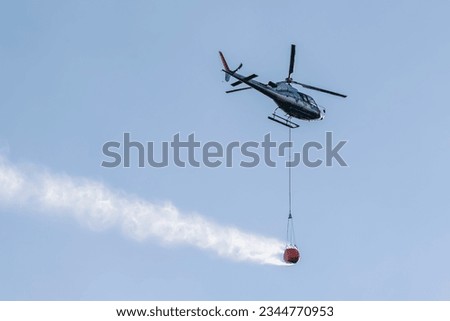 Helicopter engaged in a fire-fighting operation with the use of a large water tank attached with a rope