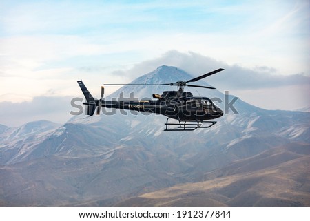Helicopter in flight. Black Helicopter is flying between mountains peak, winter time. A beautiful Caucasian mountain in the background scene. Luxury Lifestyle, Vacation tour on helicopter