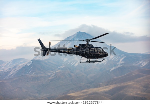 Helicopter in flight. Black Helicopter is\
flying between mountains peak, winter time. A beautiful Caucasian\
mountain in the background scene. Luxury Lifestyle, Vacation tour\
on helicopter