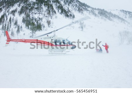 The helicopter landed people in the mountains in winter, raising a cloud of snow.