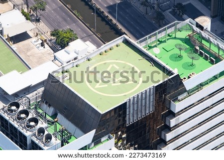 Helicopter landing pad square shape color green on top of skyscraper high. Large H shape in middle. Helipad rooftop top of building landing area in city in Bangkok. Business people or VIP guests.