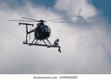 Helicopter lineman sitting on platform mounted to a helicopter as it flies overhead. - Powered by Shutterstock