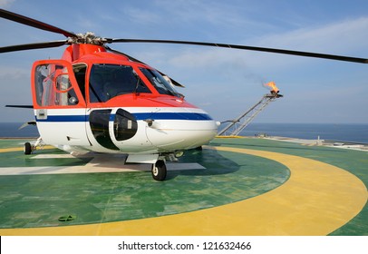 The Helicopter Park On Oil Rig To Pick Up Worker With Gas Flare And Blue Sky Backgroung