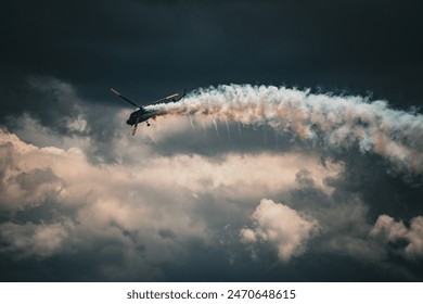 A helicopter performs an aerial stunt, trailing smoke against a dramatic, cloudy sky. - Powered by Shutterstock