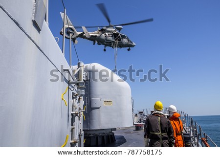 a helicopter provides the defense of a military warship. boarding of a vessel. sailors watch a helicopter dip over a ship. military drill and rescue operation.