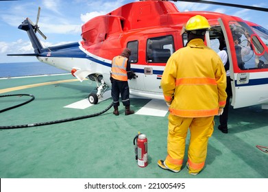 The helicopter is refueling on the helideck with a fireguard standing by