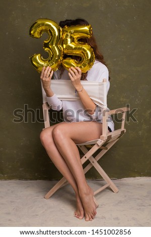 Helium balloons number 35. Young woman posing with gold foil balloons celebrating birthday