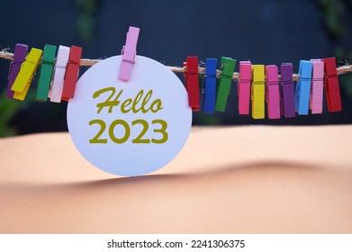 Hello 2023. New Year 2023 concept with golden text on white circle paper and colorful wooden clips on rope on dark and light orange background. Fresh hello 2023. Happy New Year.