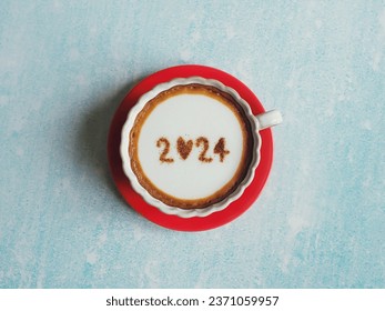 Hello 2024 theme white coffee cups with number 2024 over frothy surface placed over red saucer flat lay on pastel blue background. Holidays food art Happy New Year. (top view) - Powered by Shutterstock