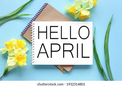 Hello April . text on white notepad paper on blue background. near notepad with yellow flowers and green leaves - Shutterstock ID 1932314801