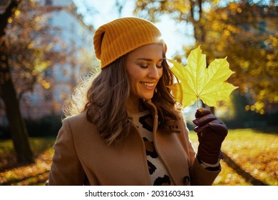 Hello Autumn. Happy 40 Years Old Woman In Brown Coat And Yellow Hat With Autumn Yellow Leaves Outside In The City In Autumn.