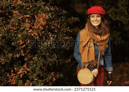 Hello autumn. happy trendy 40 years old woman in jeans shirt and red hat with scarf, gloves and bag in the city park.