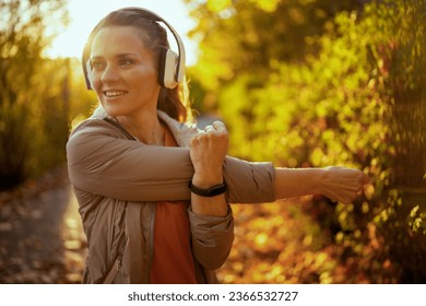 Hello autumn. happy trendy woman in fitness clothes in the park listening to the music with headphones and stretching. - Shutterstock ID 2366532727